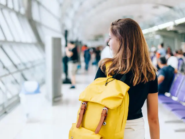 A student walking through the airport with yellow backpack.