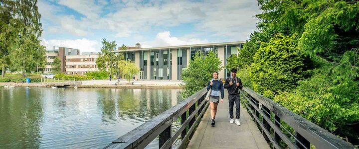 Two students walk across the bridge over the Loch, Edinburgh Campus
