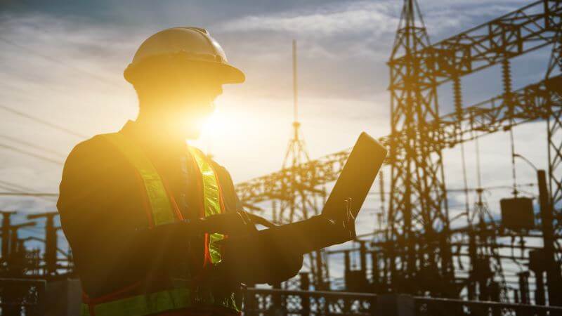 Man in construction outfit holding tablet with crane in background