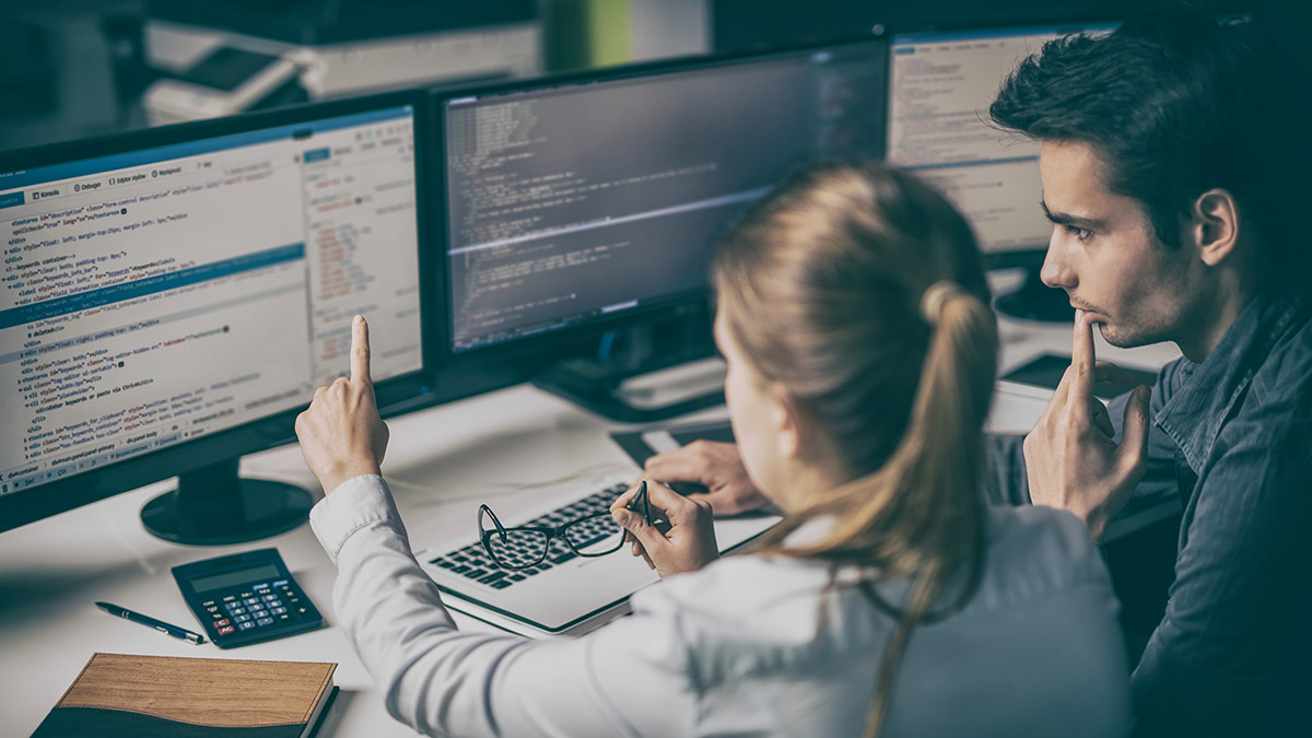 Two students discuss computer code on a monitor