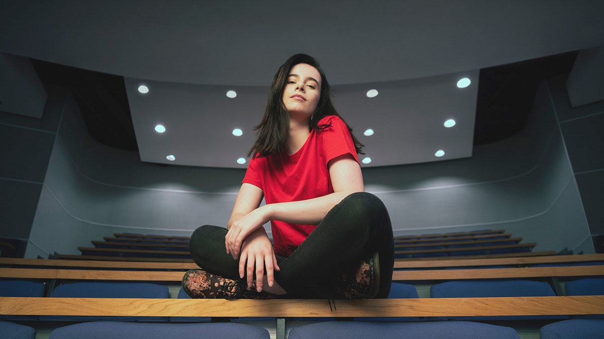 Female student sitting cross-legged on a lecture theatre desk