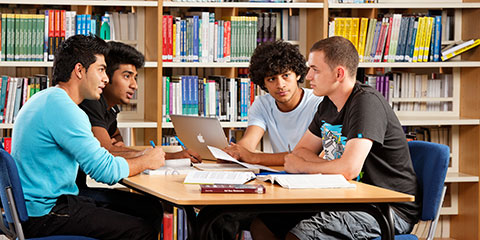 Four male students in discussion at a table in the Library