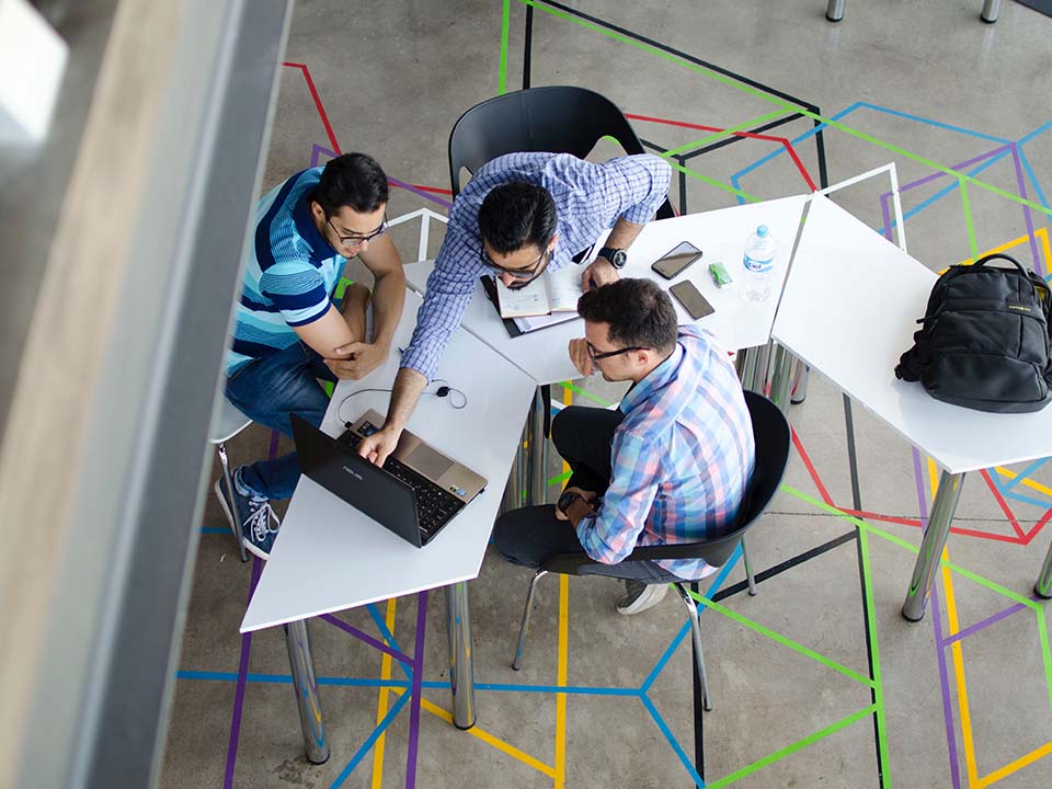 Group of male students working around an angular table, viewed from above