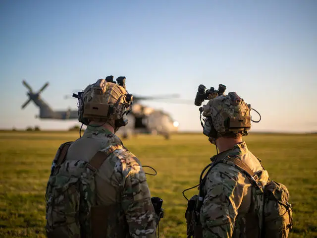 Two armed forces personnel look towards an RAF helicopter during a military exercise