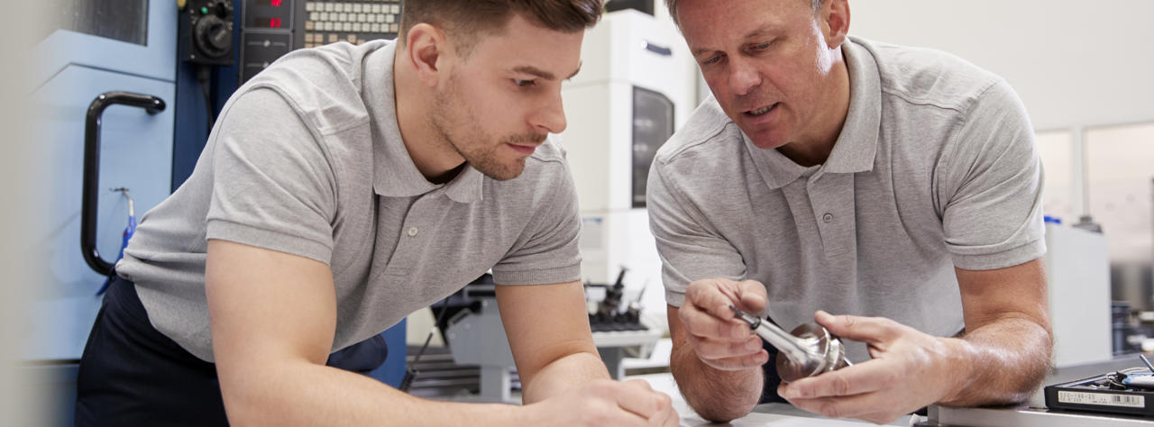 Apprentice and manager inspecting a component in the workplace.