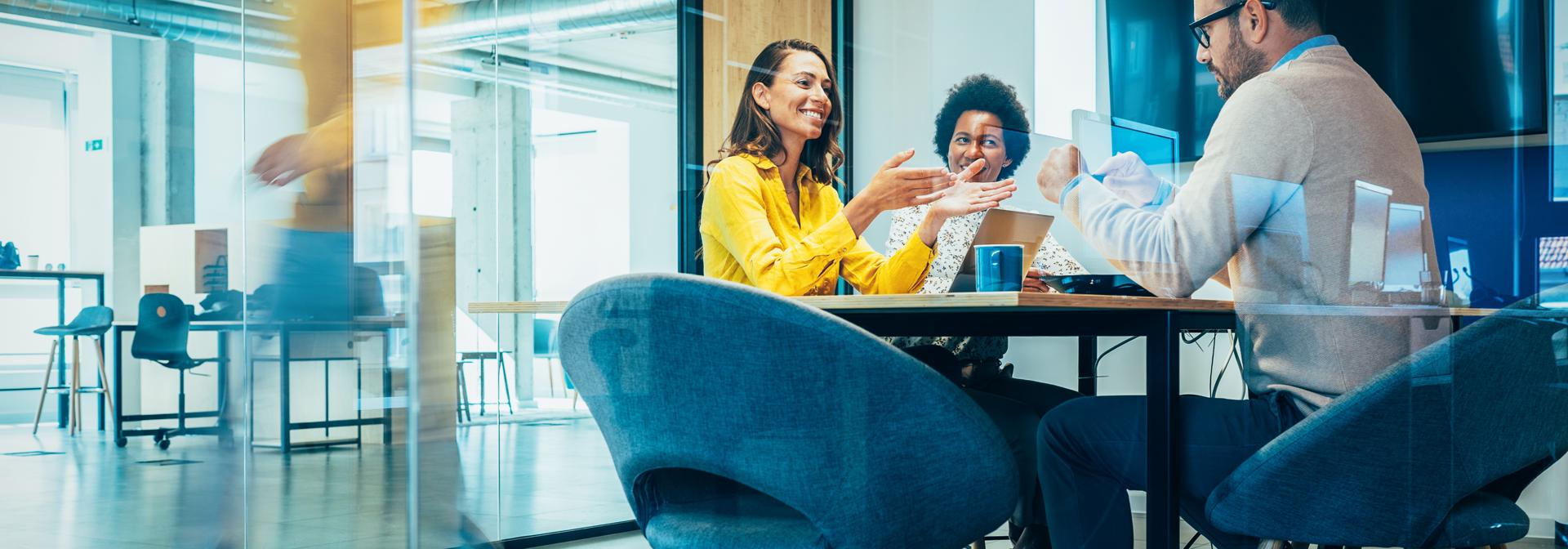 Three people seated at a meeting table in a business office.