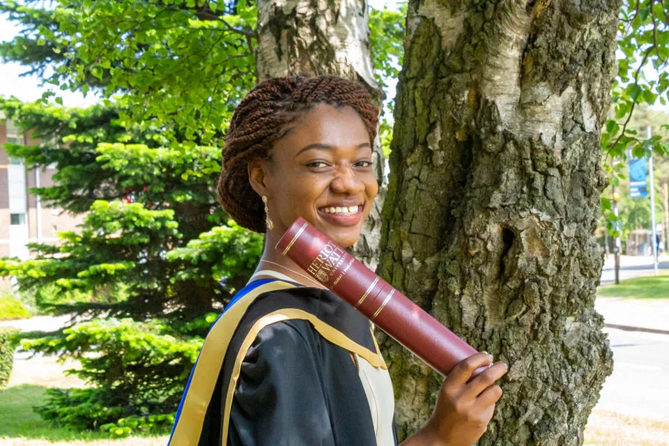 A student wearing the graduation robes and holding a scroll