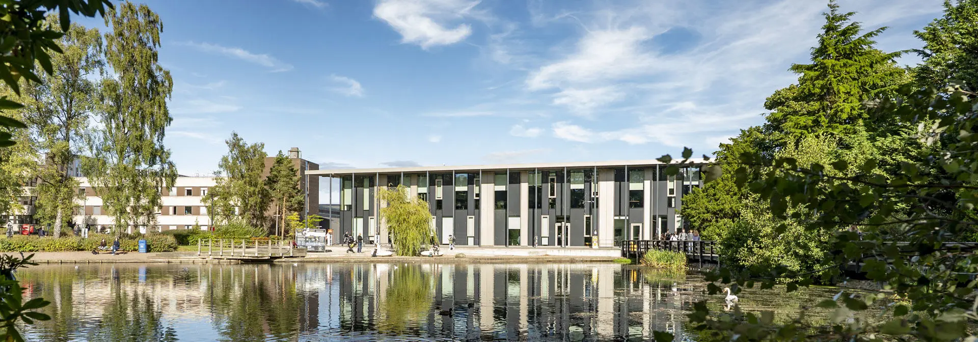 The GRID building stands behind a serene Loch, reflecting its structure in the calm water.