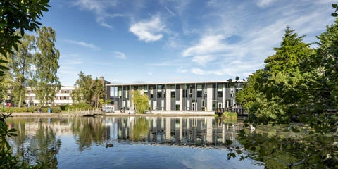 The GRID building stands behind a serene Loch, reflecting its structure in the calm water.