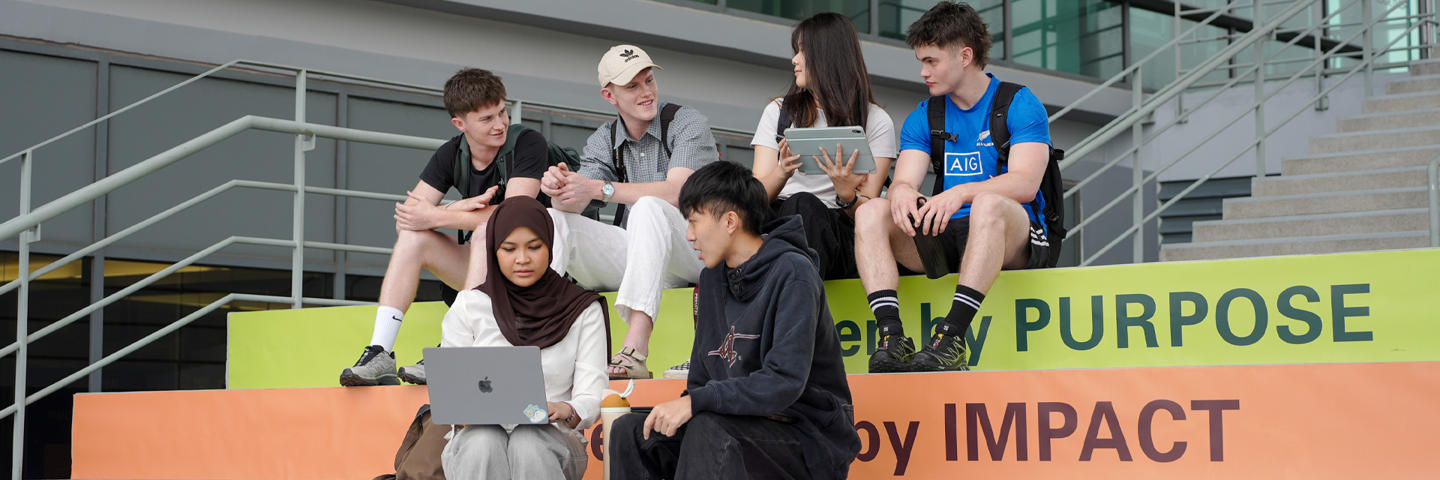 Students sit on colorful steps, engaged with laptops and tablets, in a modern outdoor setting.