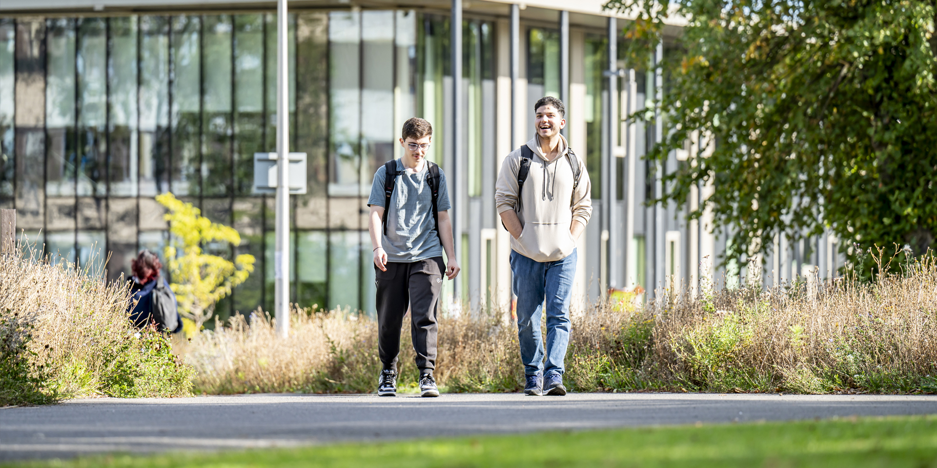 Two students walking and talking on a sunny paved path near the GRID building.