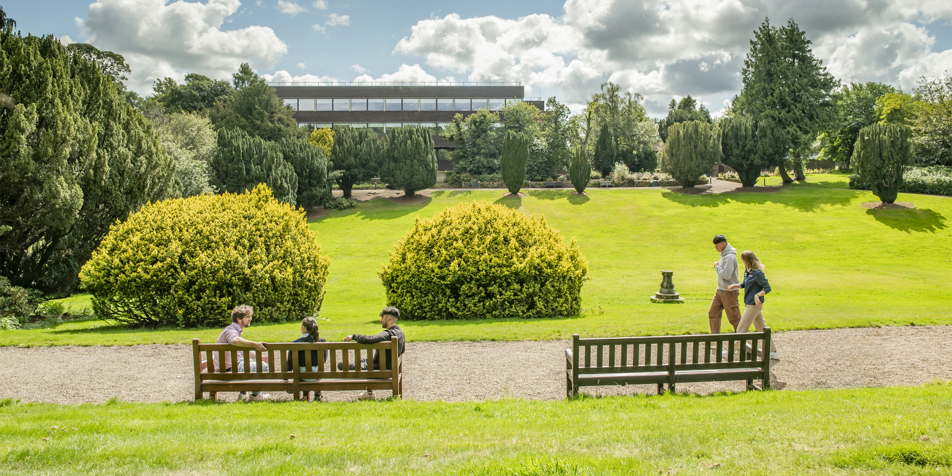 Students chat whilst enjoying the campus in the sunshine