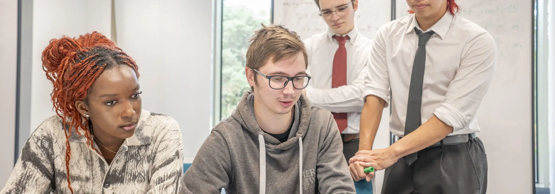 Four students collaborate on a laptop in a modern office setting, focused on their work and sharing ideas.