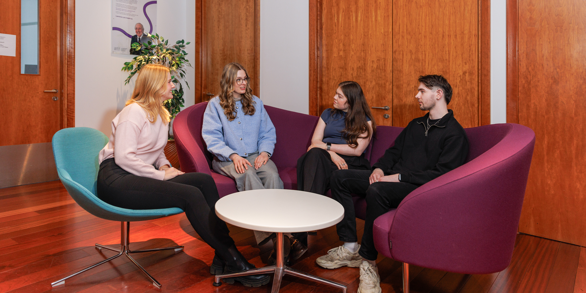 A group of four students sit together in modern chairs, engaging in conversation in a cozy setting.