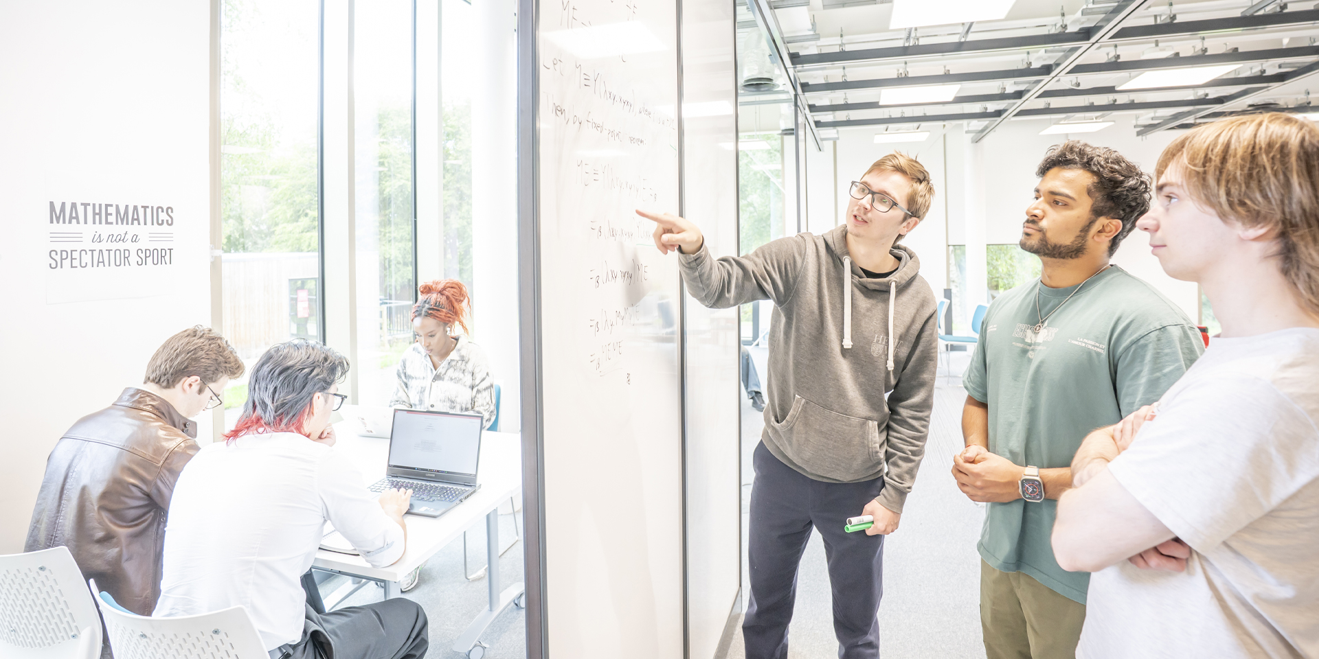 Students collaborate around a whiteboard filled with mathematical equations, while another group works nearby.