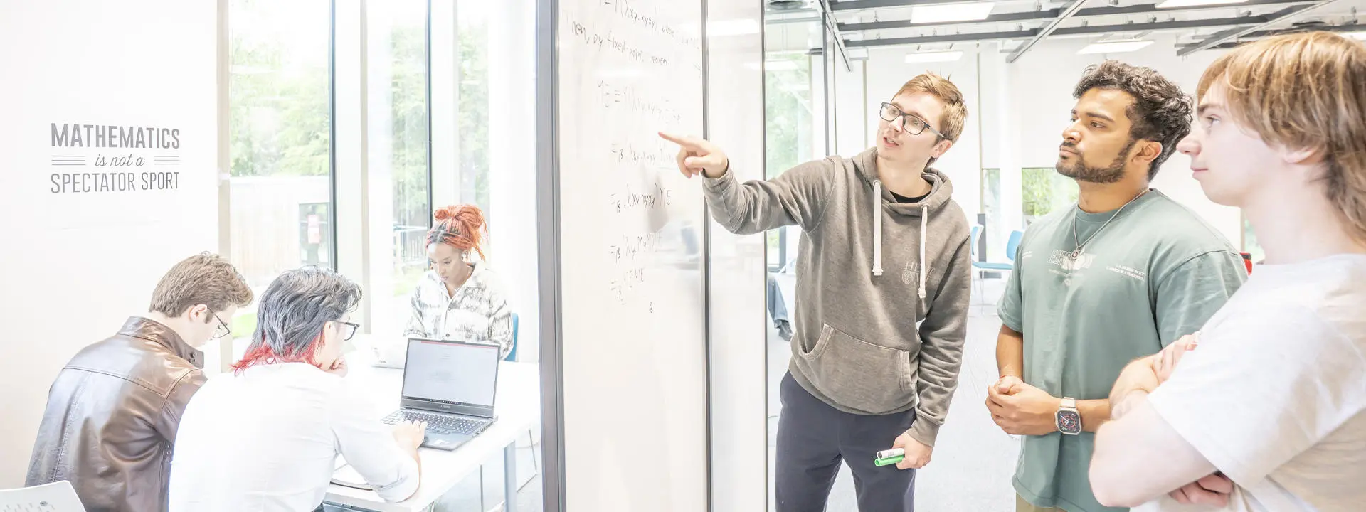 Students collaborate around a whiteboard filled with mathematical equations, while another group works nearby.