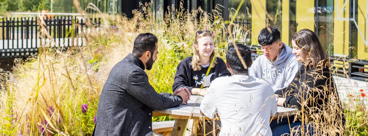 Students sitting around a wooden picnic table outdoors, engaged in conversation.
