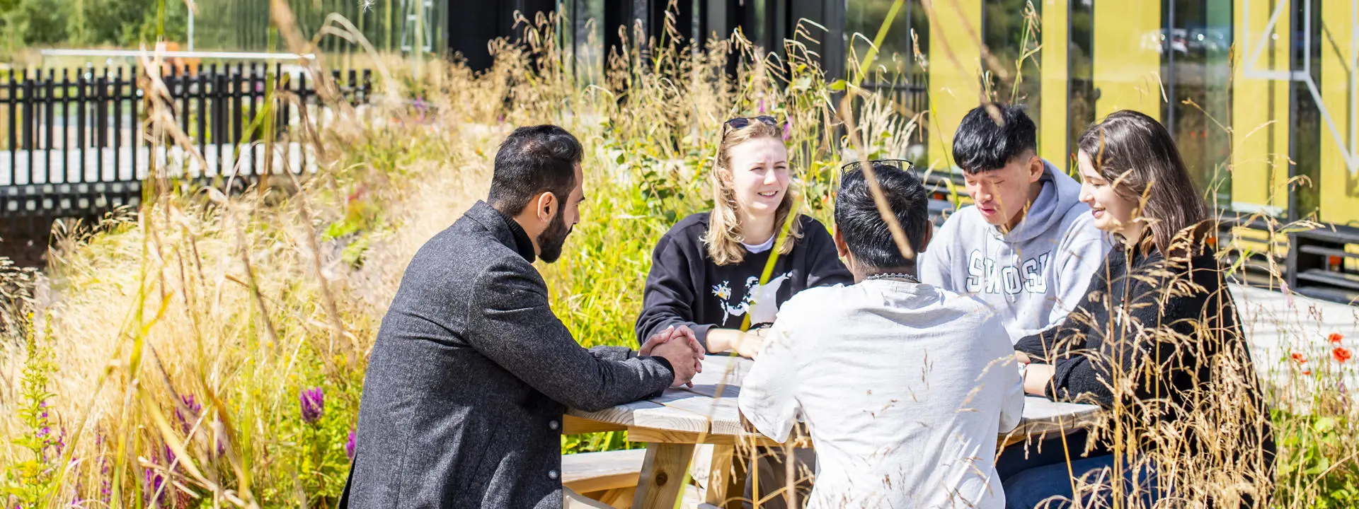 Students sitting around a wooden picnic table outdoors, engaged in conversation.