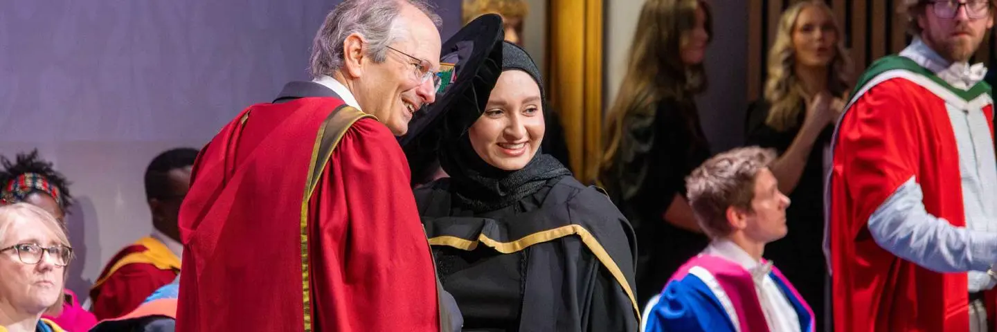 A woman and a man wear graduation gowns, smiling proudly as they commemorate their graduation day.