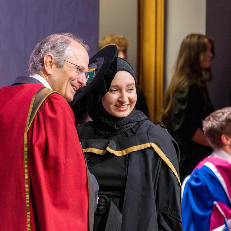 A woman and a man wear graduation gowns, smiling proudly as they commemorate their graduation day.