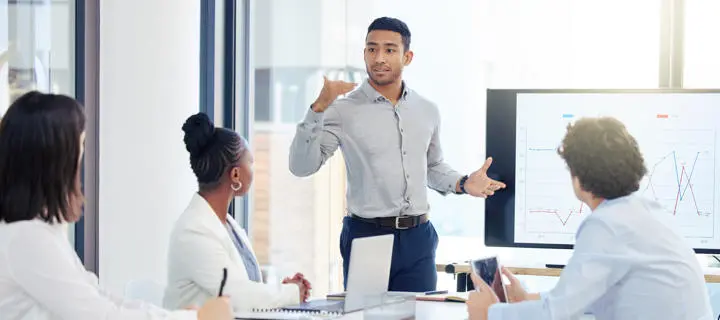 A man presenting to a group of colleagues in a conference room, engaging them with visual aids.