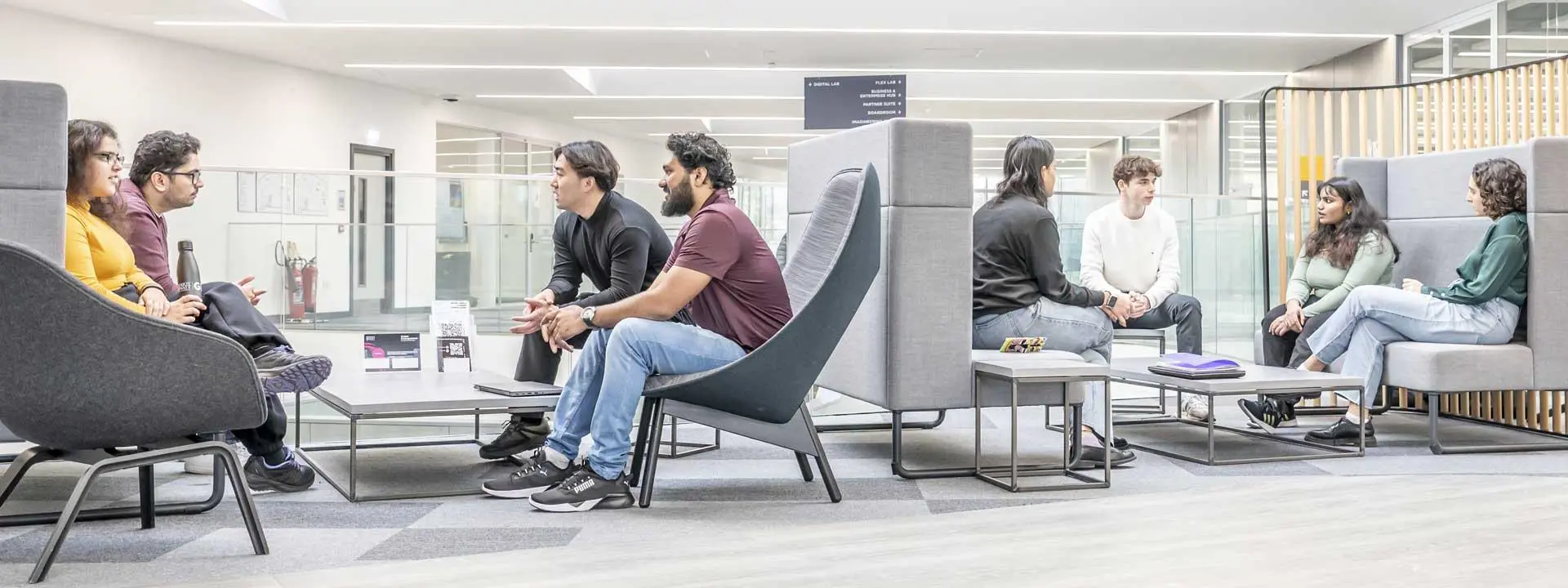 Two groups of students sitting in booths talking in a modern building.