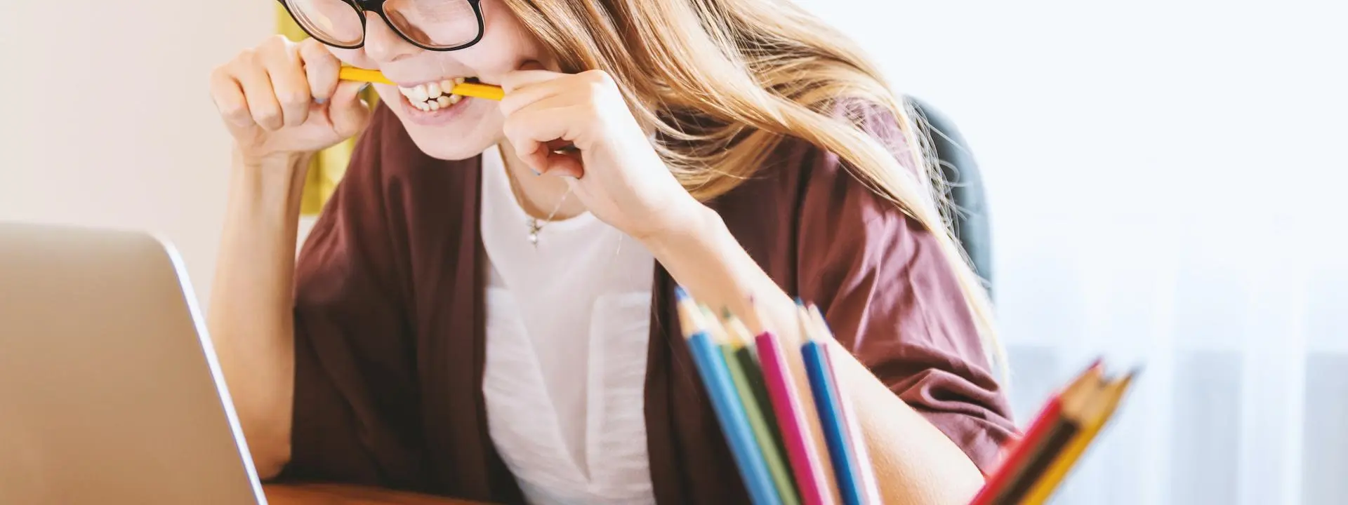 A woman bites her pencil in frustration while looking at her laptop screen