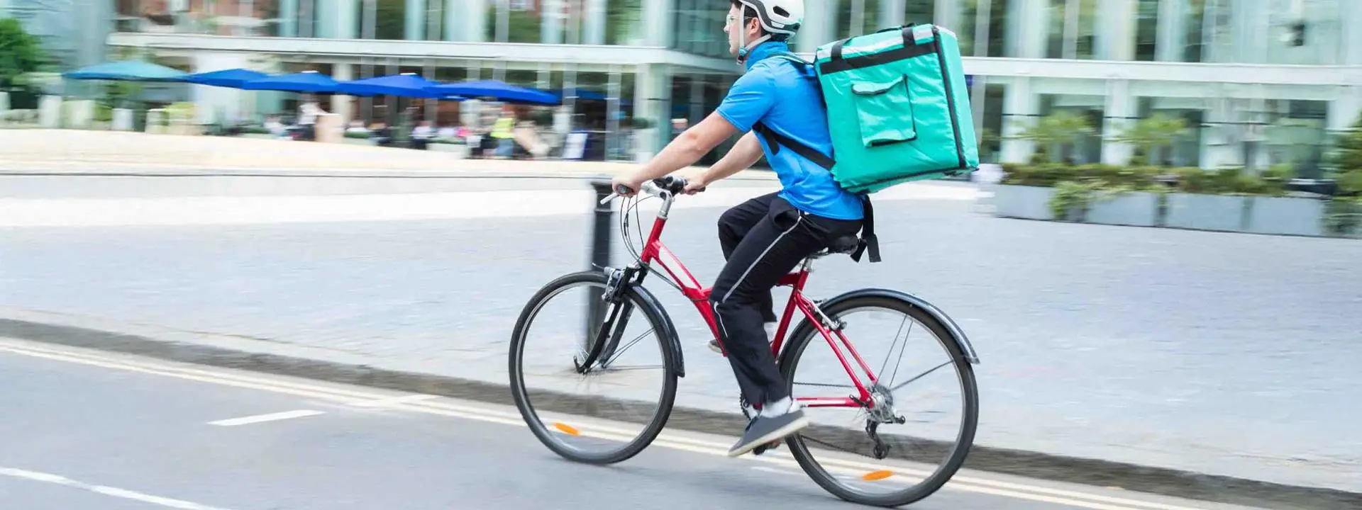 Food delivery rider on a bicycle, carrying a large bag on his back, navigating a city street.