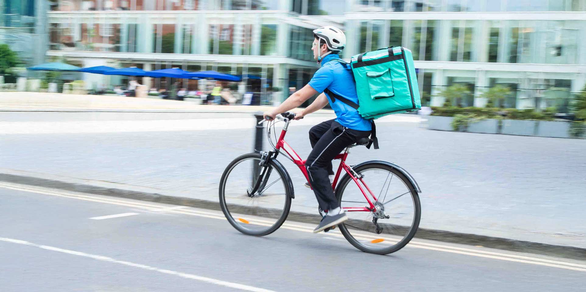 Food delivery rider on a bicycle, carrying a large bag on his back, navigating a city street.