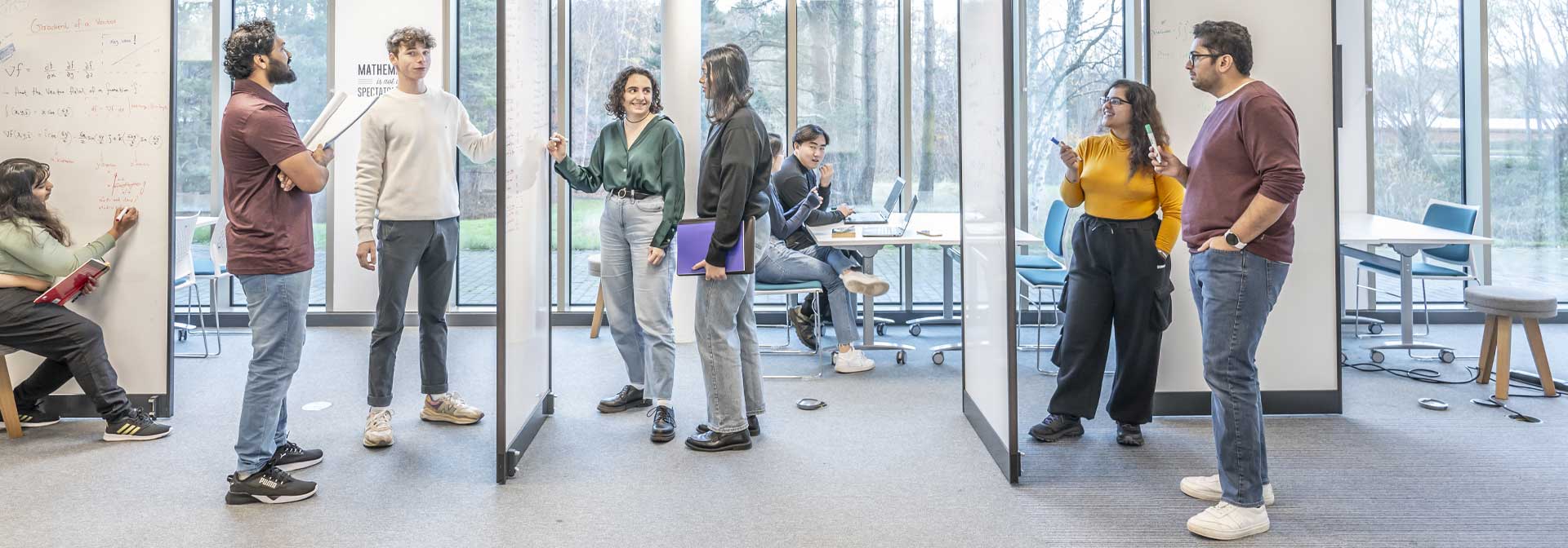 A group of students engaged in conversation beside a whiteboard within a modern learning environment.