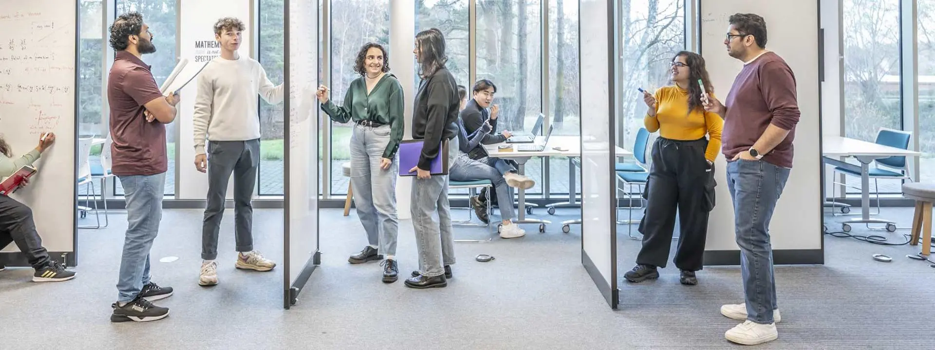 A group of students engaged in conversation beside a whiteboard within a modern learning environment.