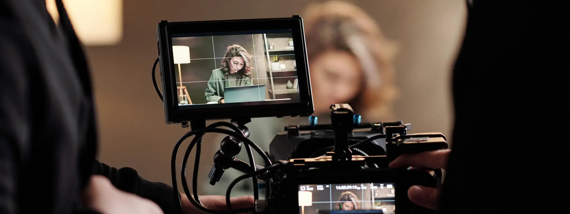 A woman working on a laptop is filmed by a professional video crew.