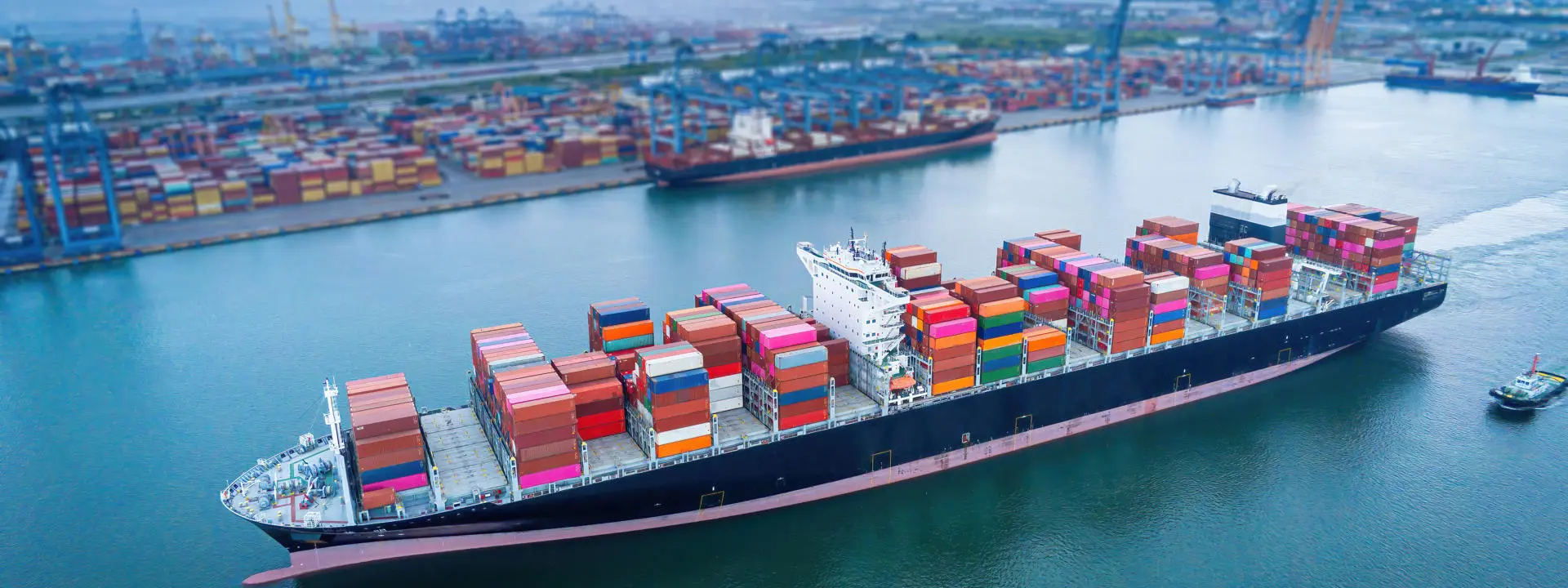 Cargo ship carrying multicoloured shipping containers arriving at a busy port..
