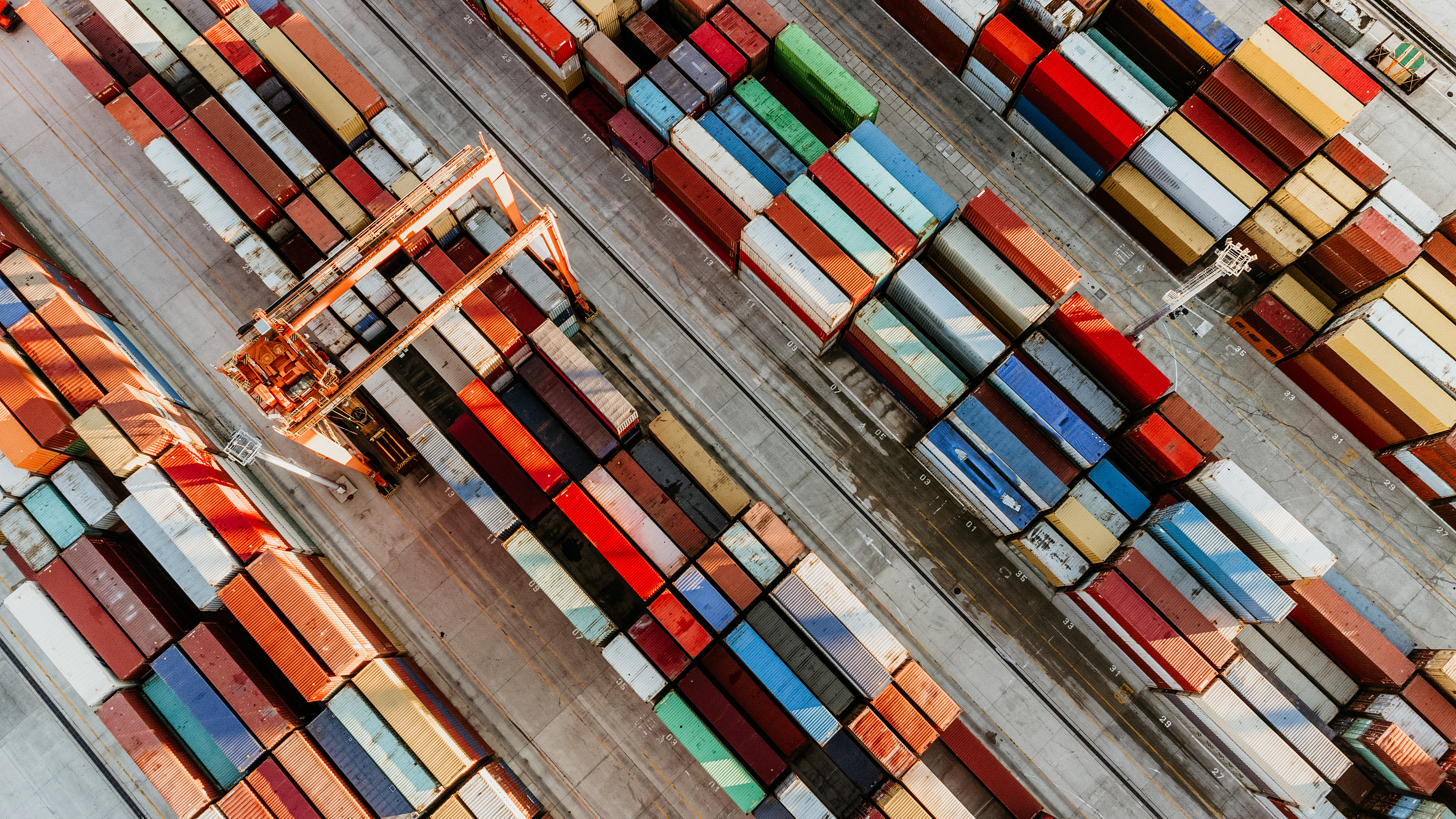 Aerial view of a shipping yard with rows of colourful cargo containers and cranes arranged in an orderly pattern.