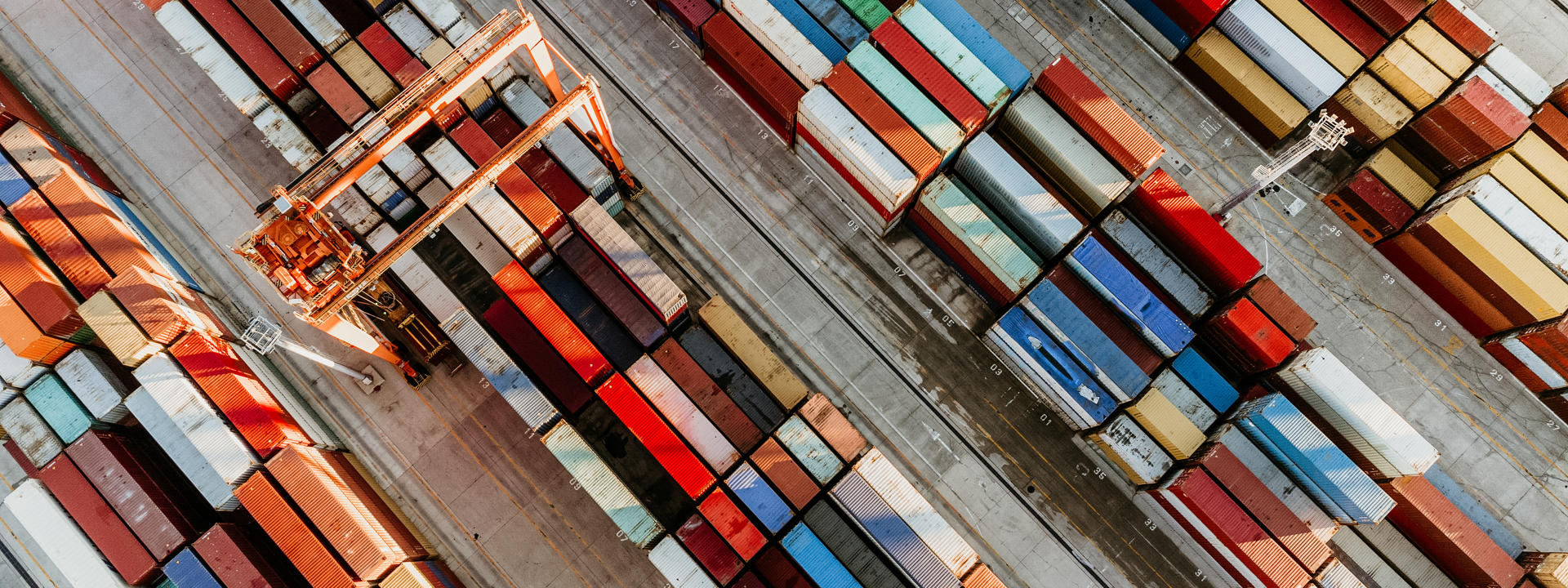 Aerial view of a shipping yard with rows of colourful cargo containers and cranes arranged in an orderly pattern.