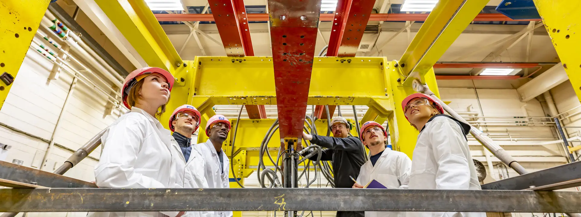 Five students standing inside a large piece of equipment, looking up while a member of staff speaks