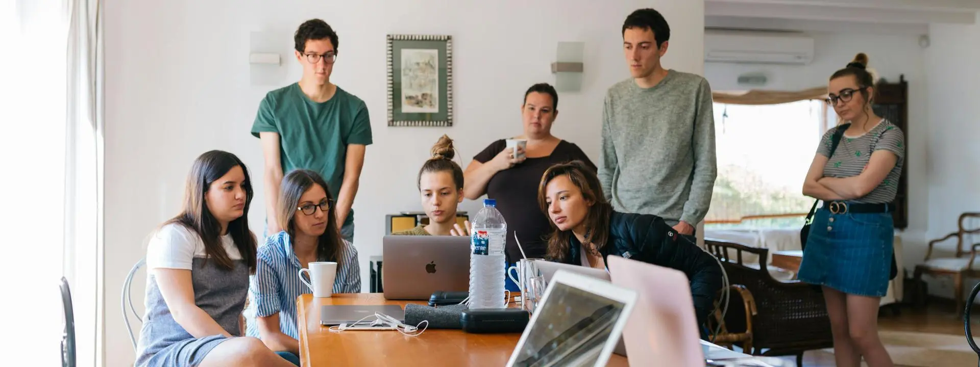 A group of people gathered around a woman with a laptop computer on a table