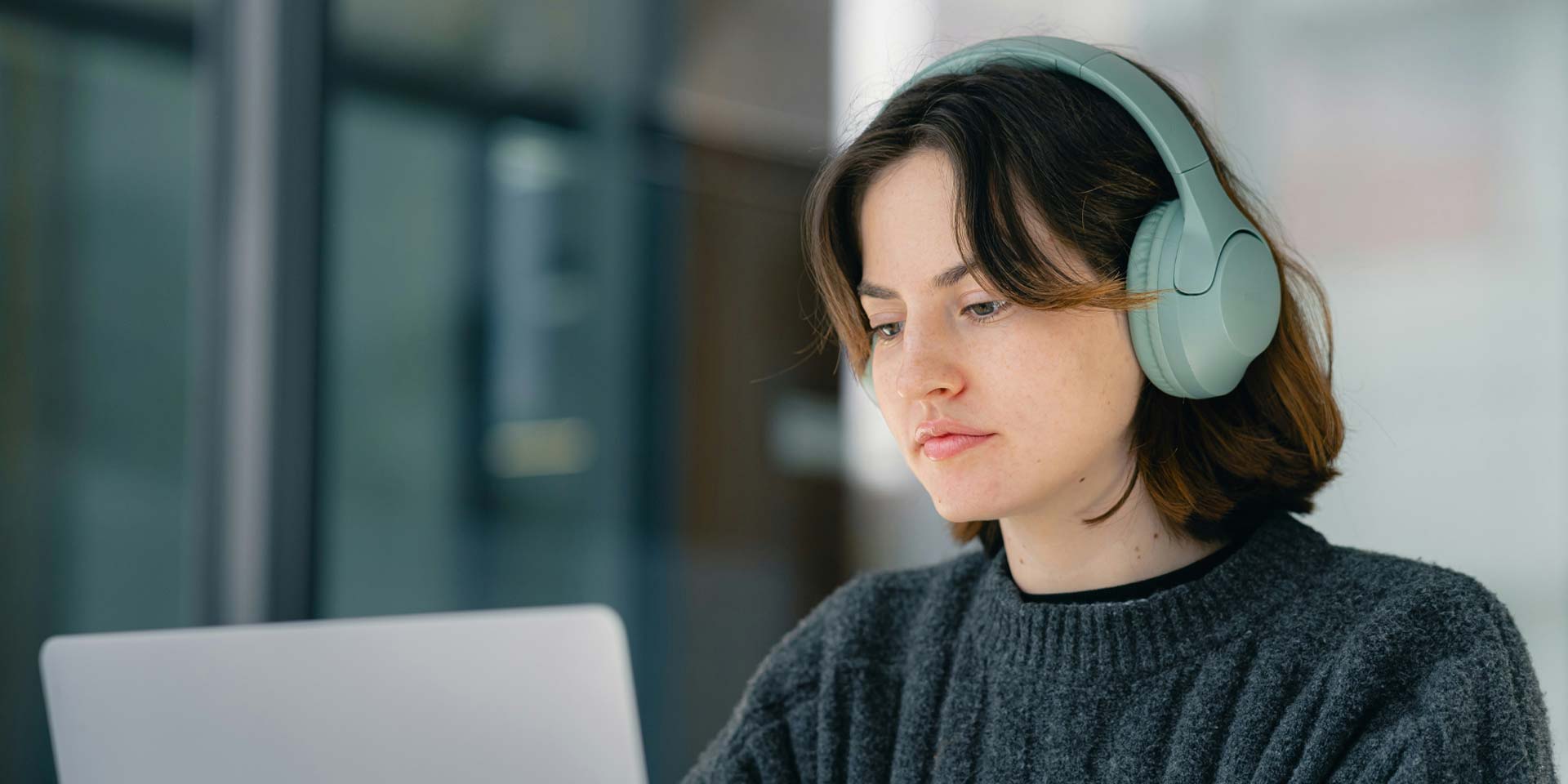 A student with headphones sits at a desk, focused on her laptop while studying.