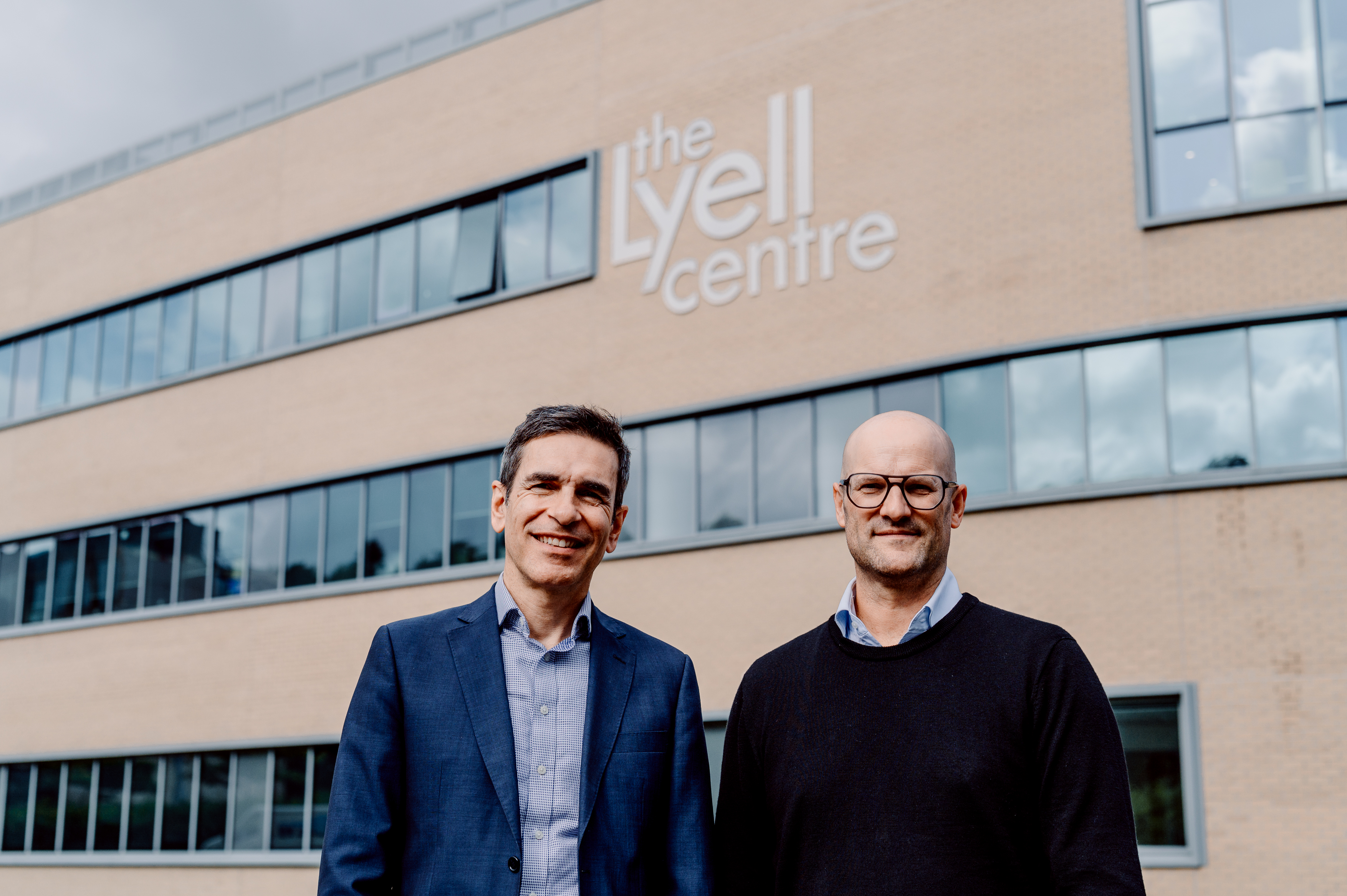 Two men stand in front of the Lyell Centre building. It is a large brick building with lots of windows.