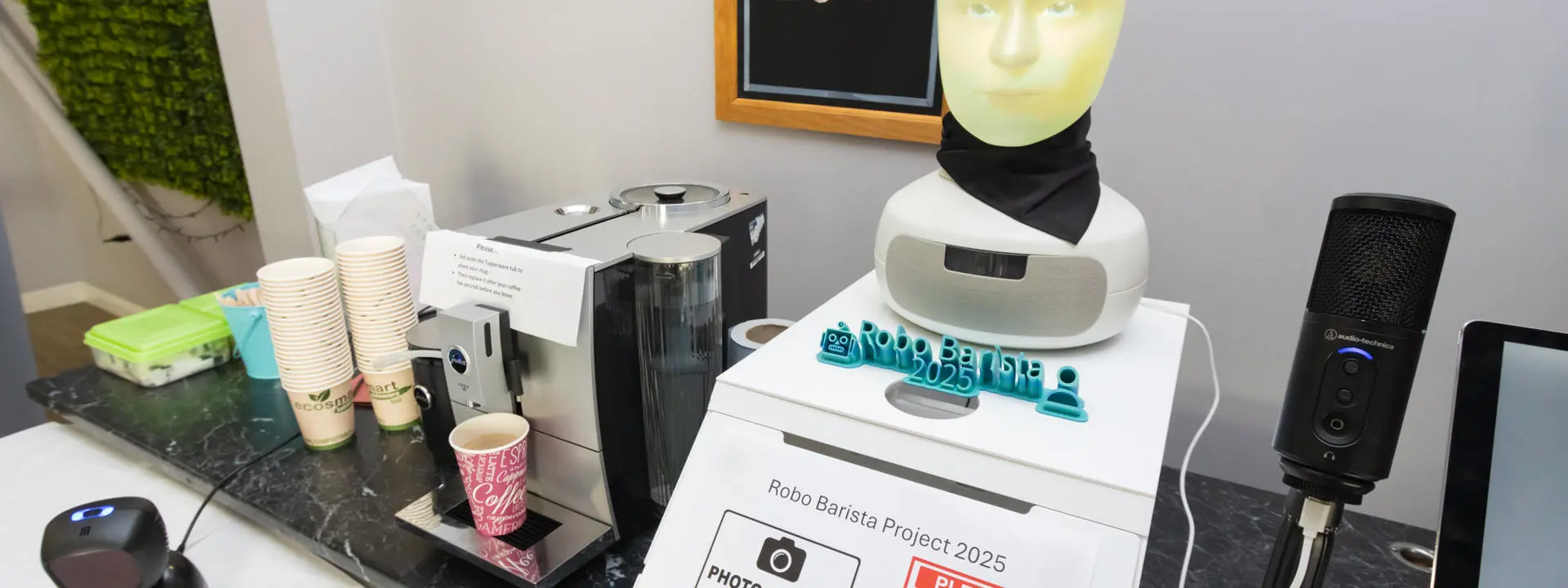 A humanoid robot barista setup at a coffee station, featuring a coffee machine, microphone.