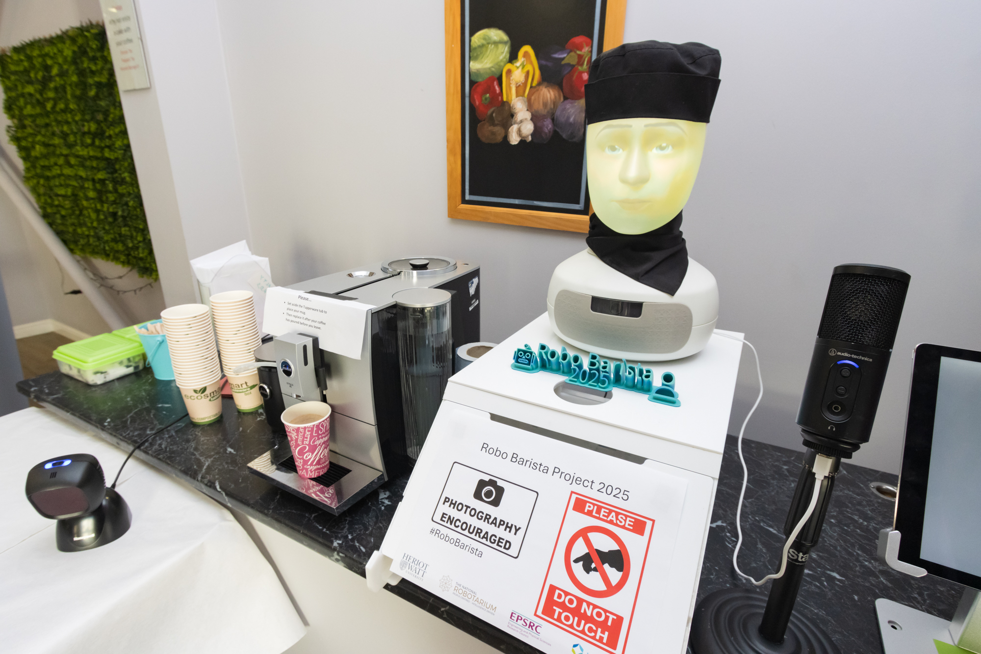 A humanoid robot barista setup at a coffee station, featuring a coffee machine, microphone. 