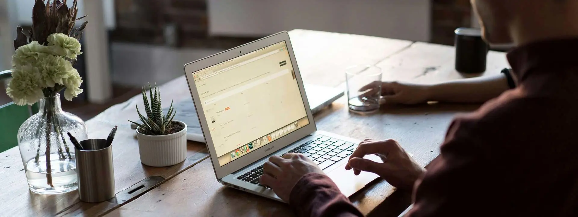 A man seated at a desk, focused on his laptop, with a notepad and pen beside him.