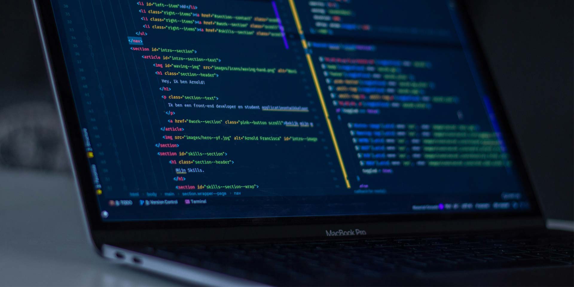 A laptop with programming code on its screen rests on a desk.