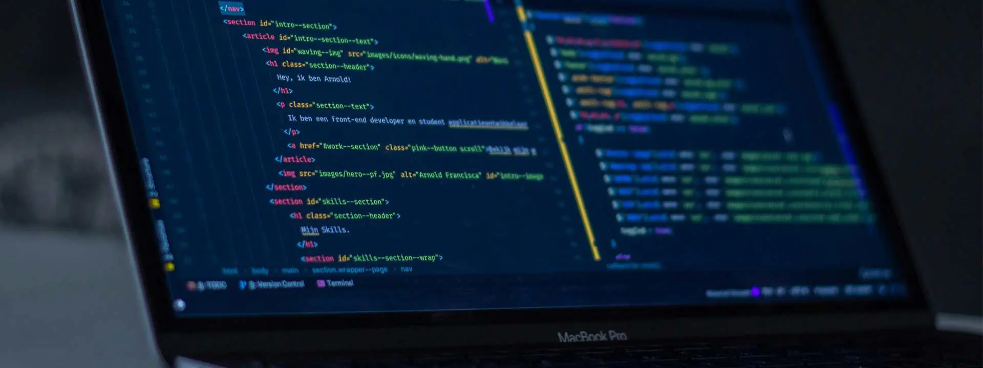 A laptop with programming code on its screen rests on a desk.
