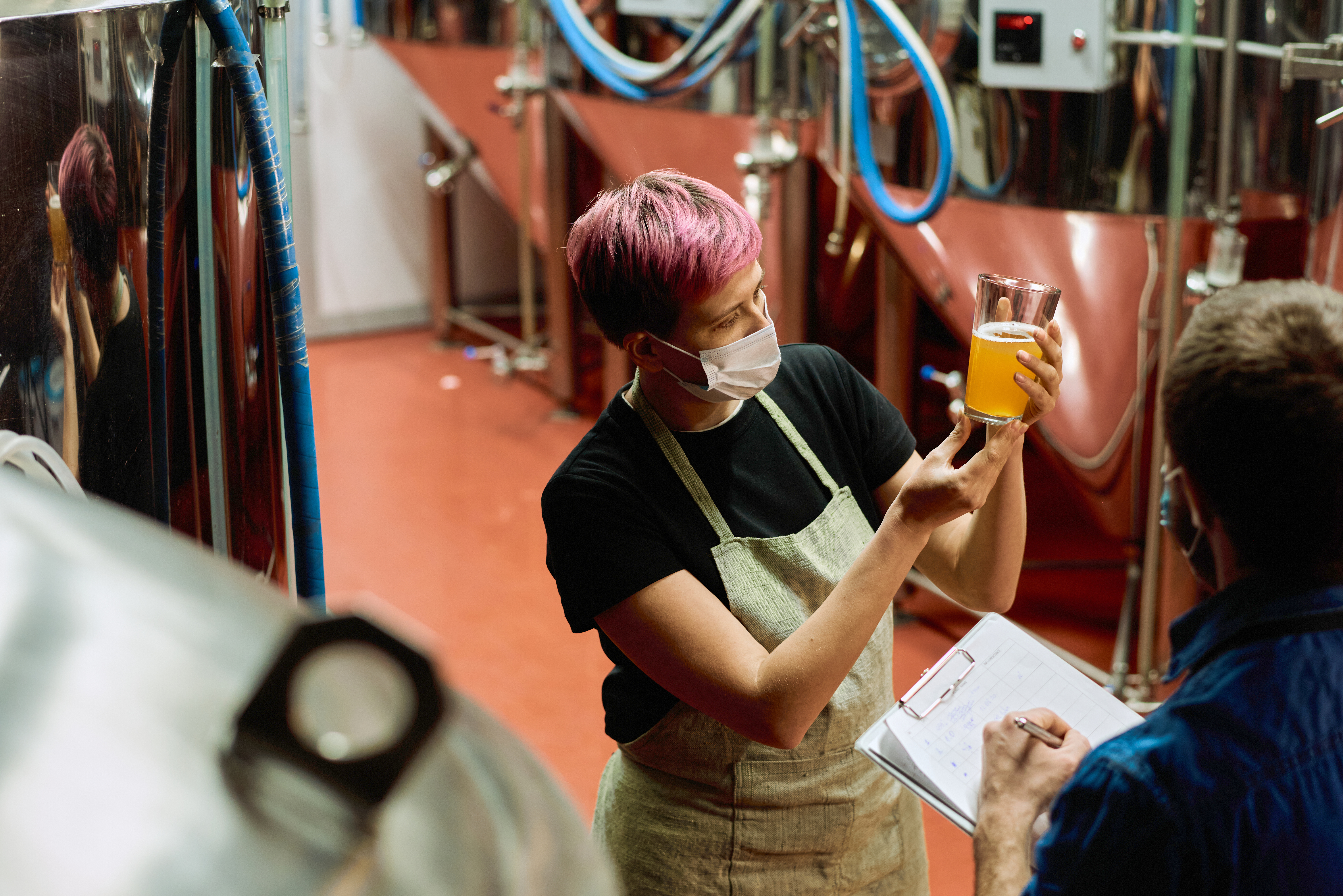 A person visually inspecting a glass containing a brewed, malted beverage