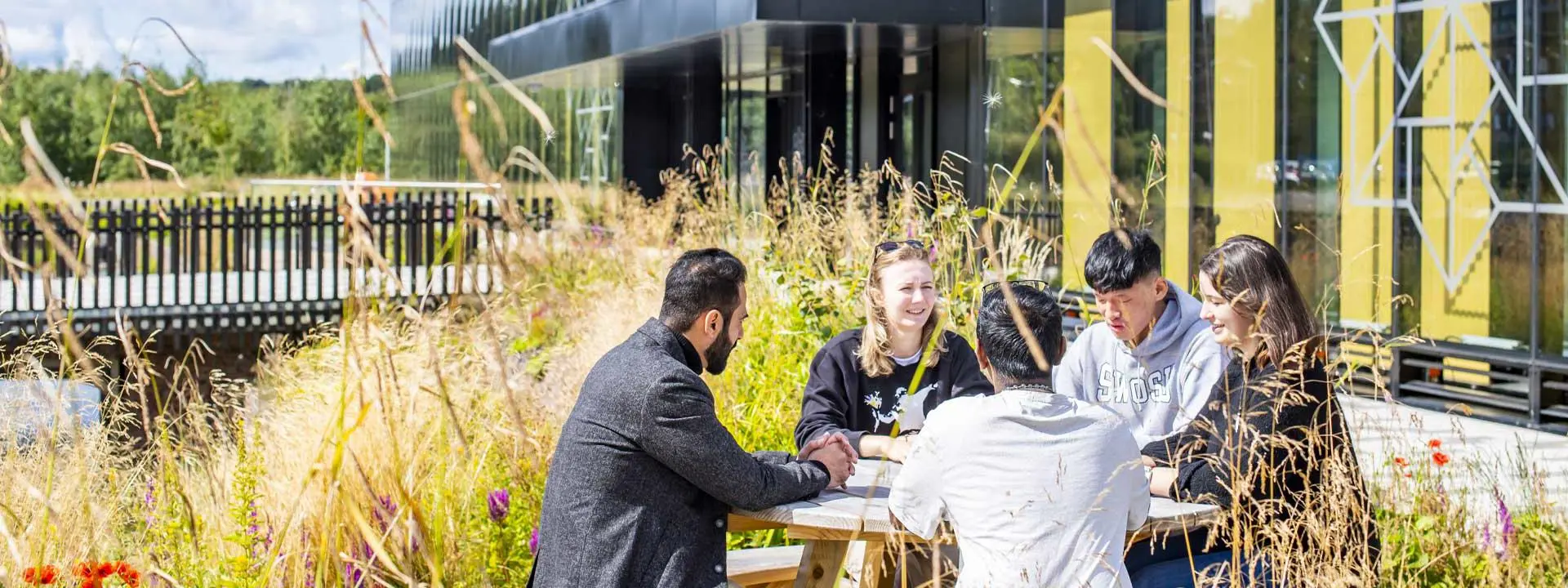 Five people sitting at a round table outside the National Robotarium on a sunny day.