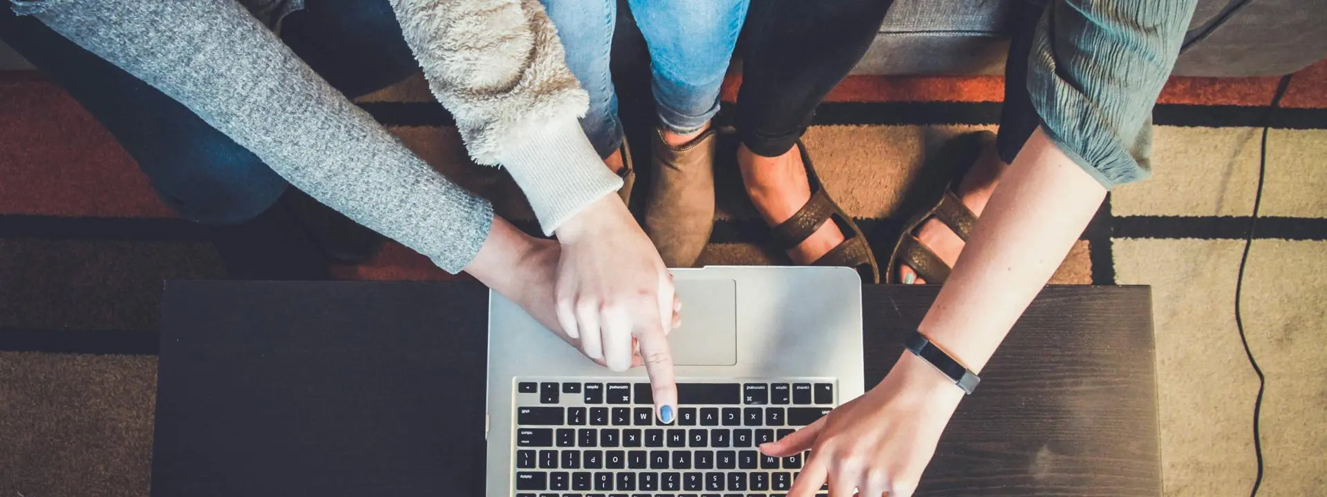 A group of women point at a laptop screen simultaneously