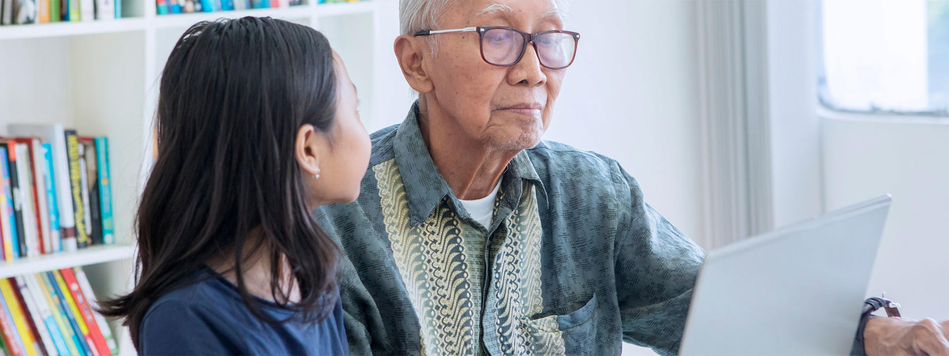 A young girl helps an old man to use a laptop computer