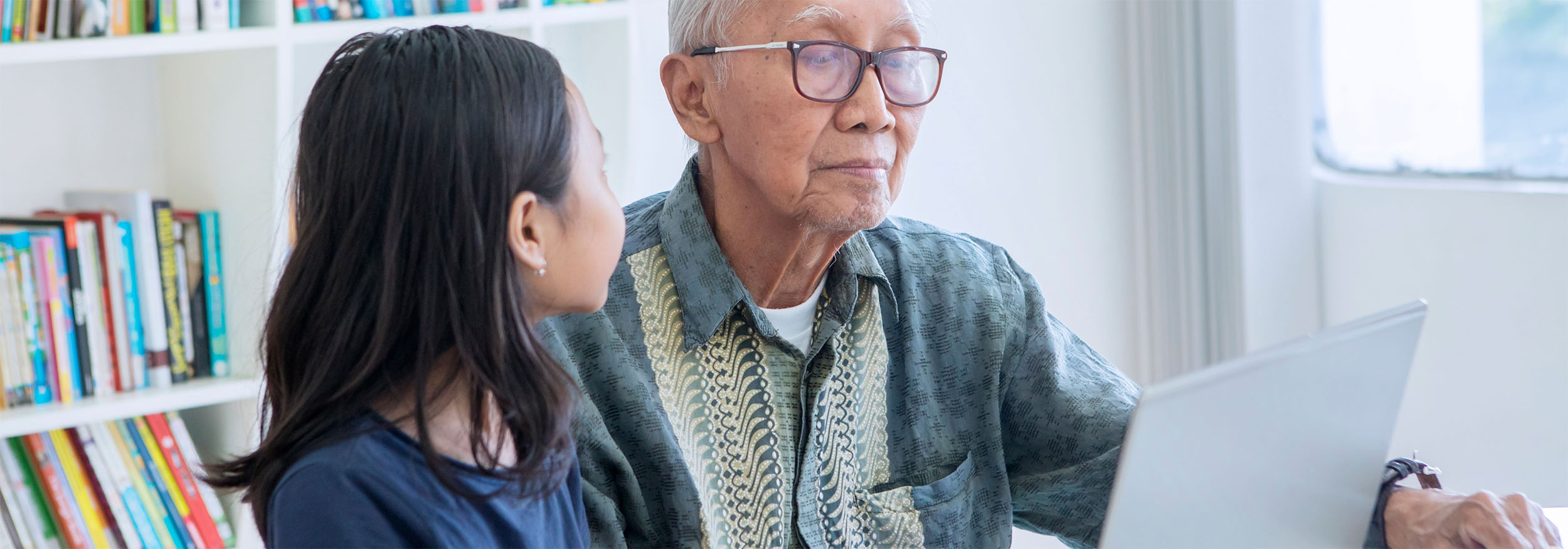 A young girl helps an old man to use a laptop computer