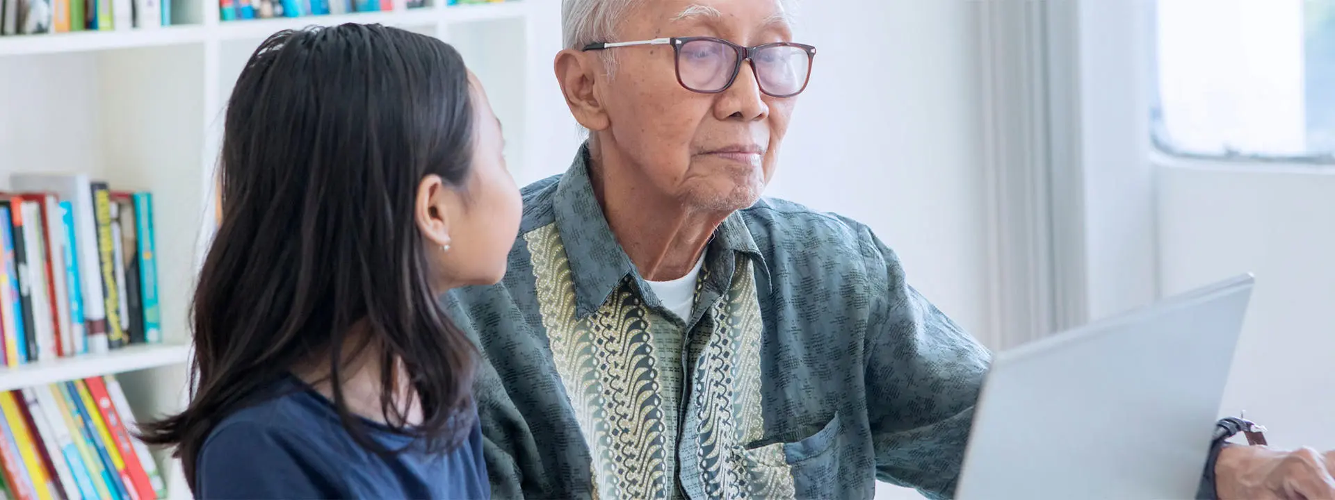 A young girl helps an old man to use a laptop computer